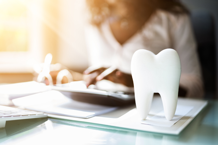 A dentist in their office typing on a keyboard, with a teeth model on the table.